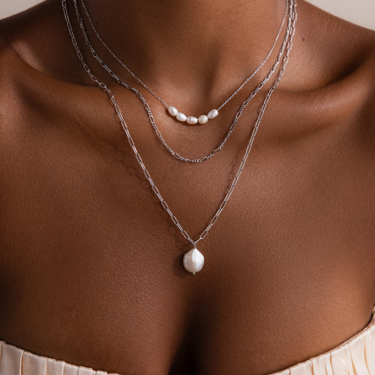 Close-up of a person wearing multiple silver necklaces on a neutral background