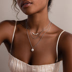 Close-up of a woman wearing layered silver necklaces with a neutral background