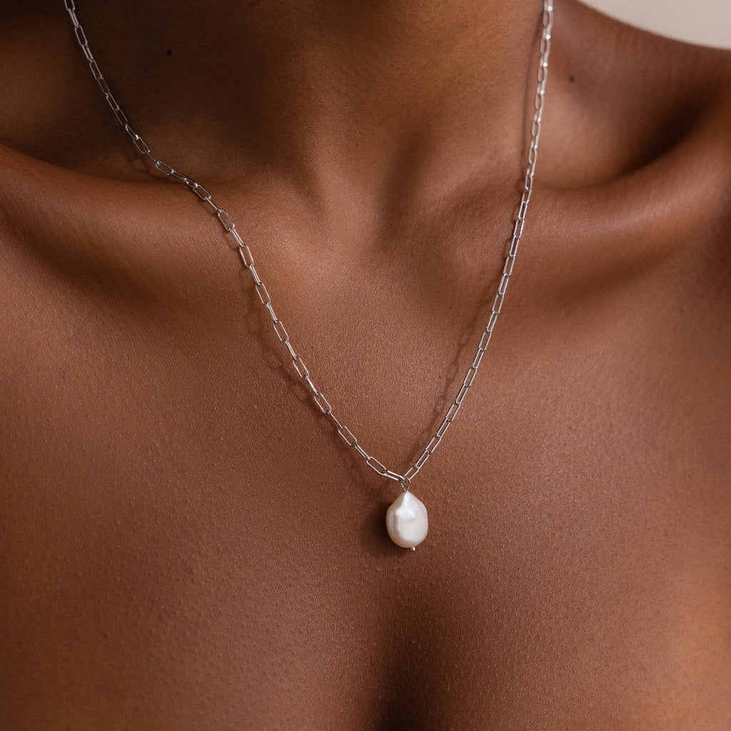 Silver paperclip chain necklace with a pearl pendant on a woman's neck