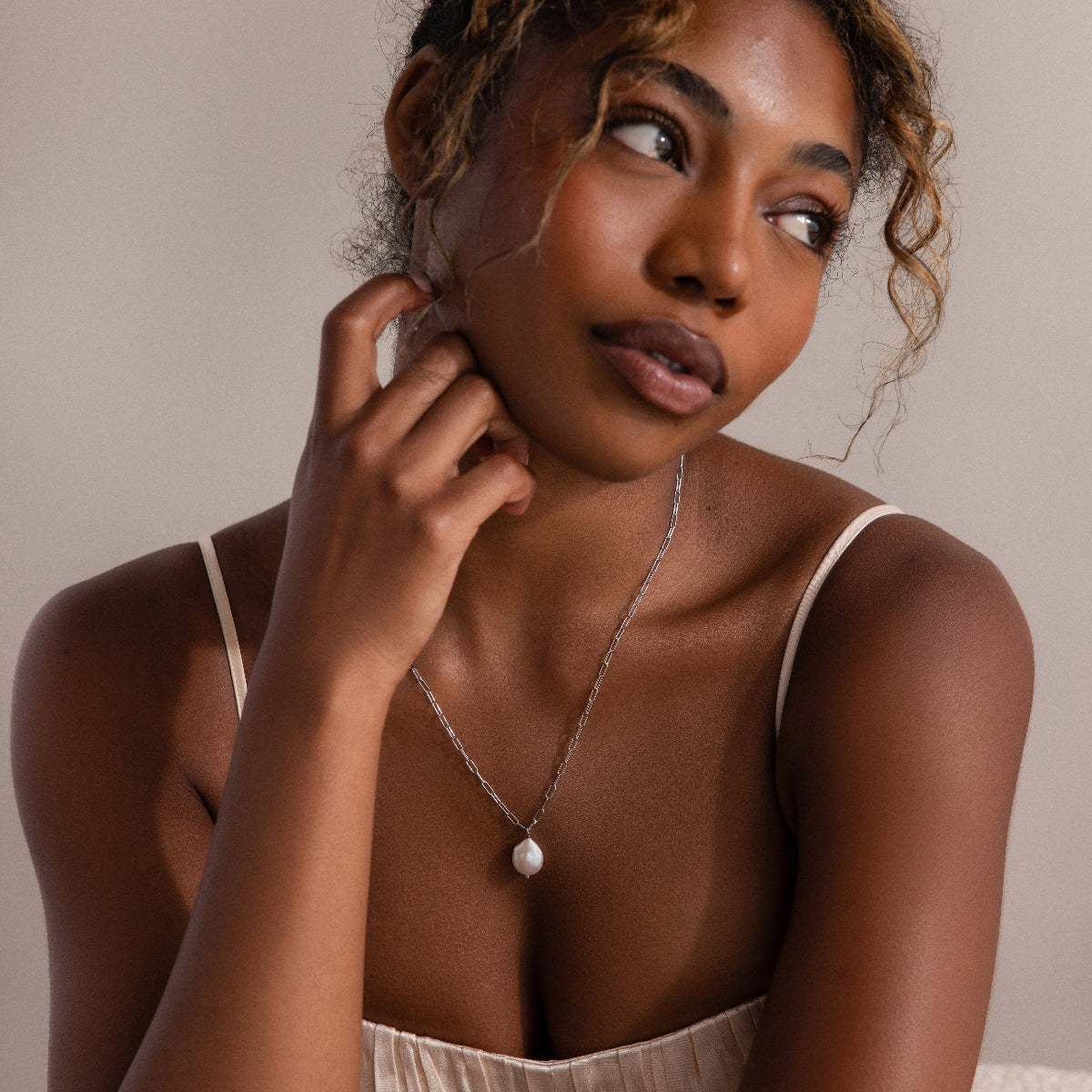 Woman wearing a silver chain necklace with a pearl pendant against a neutral background