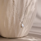 Silver link chain necklace with a pearl pendant on a beige stone background