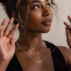 Woman holding a silver 'mama' necklace against a neutral background