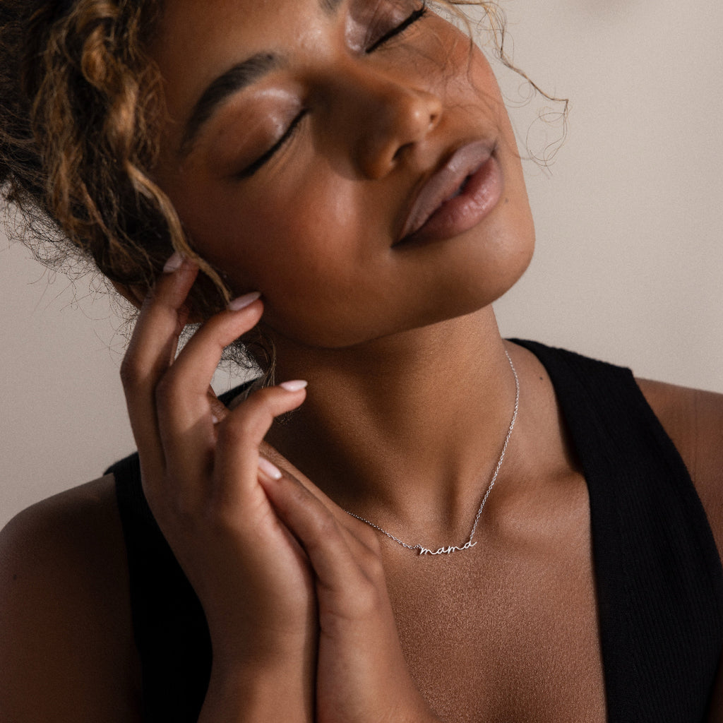 Woman wearing a silver mama charm necklace with a neutral background