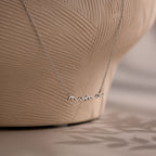 Silver necklace with 'mama' pendant on a textured beige background