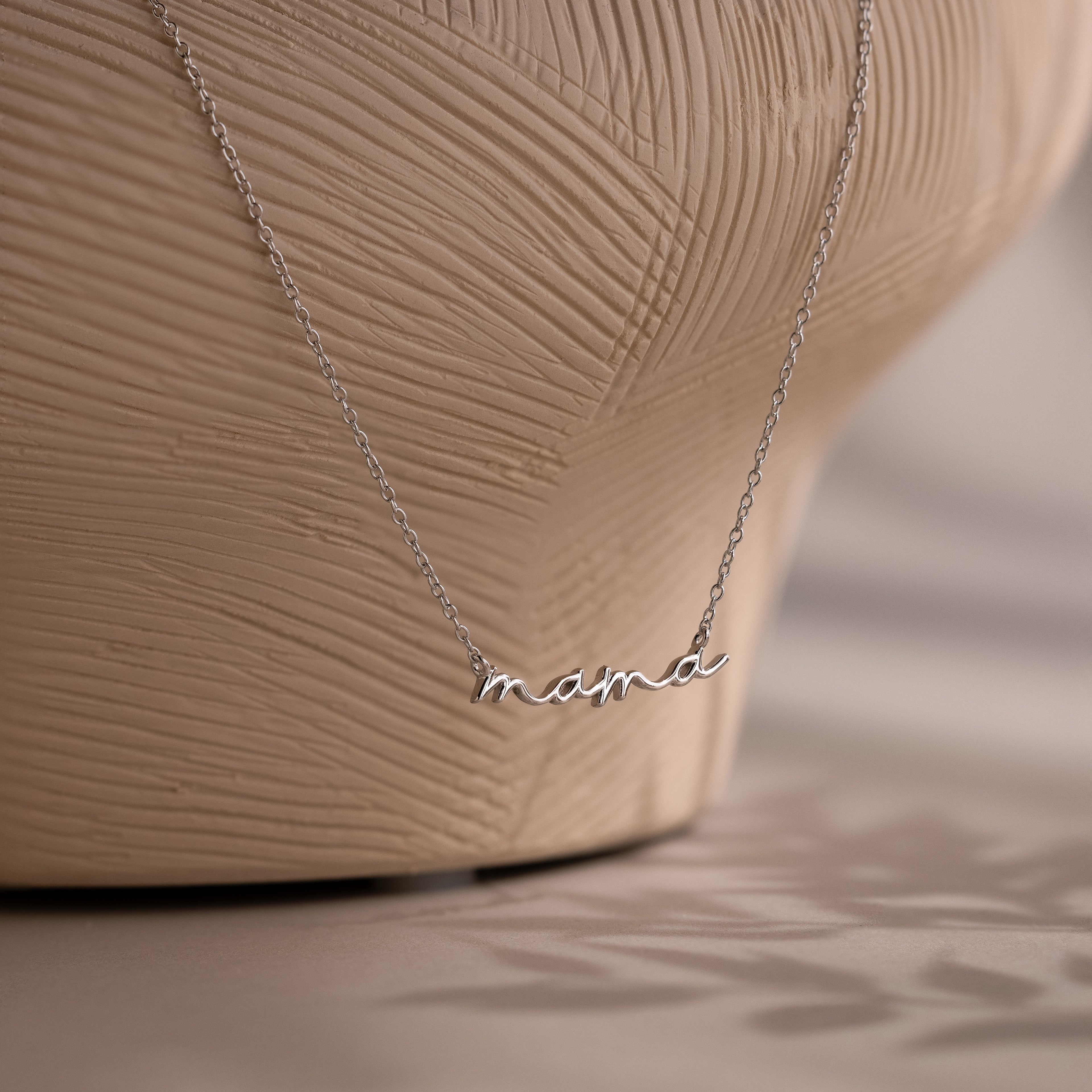 Silver necklace with 'mama' pendant on a textured beige background