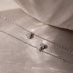 Two Diamond Station Necklaces in Silver, featuring small round diamond pendants, rest on a soft beige surface—embodying modern elegance for a timeless accessory to enhance any look.