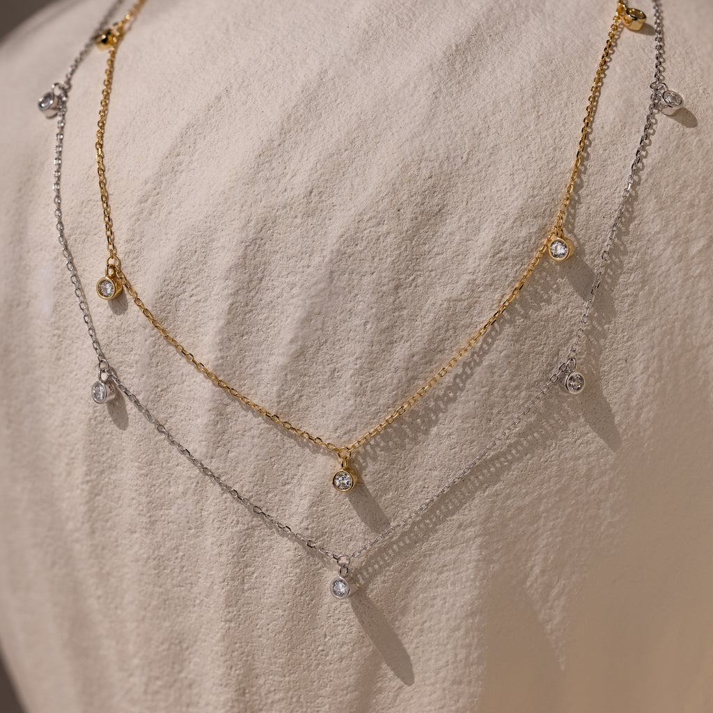 Features two gold and silver necklace chains with clear gemstone accents, creating a modern, timeless accessory that adds elegant sparkle to any outfit.