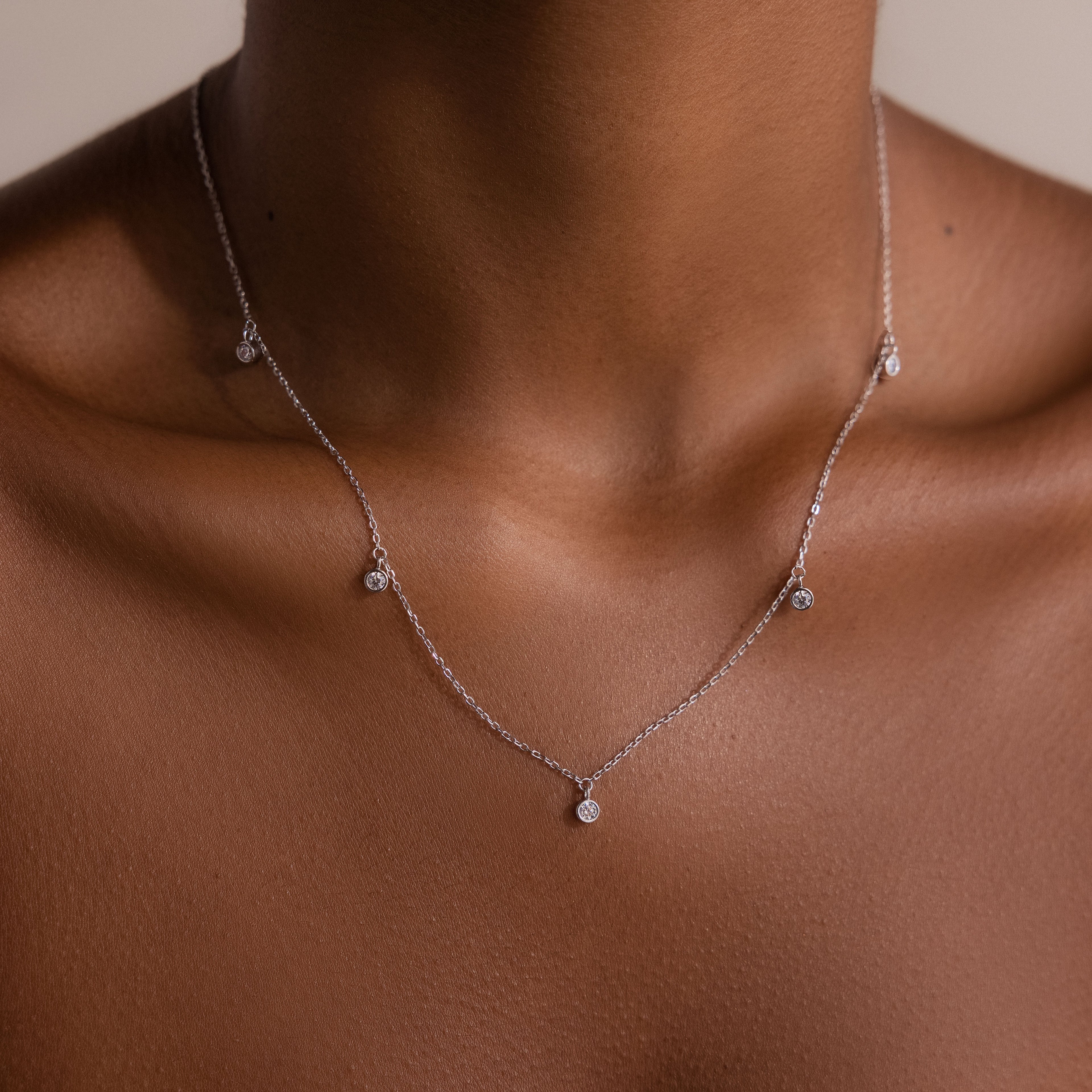 The Diamond Station Necklace features delicate silver with small round pendants, offering a touch of modern elegance and subtle charm to any neckline.
