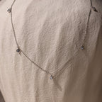 The Diamond Station Necklace in Silver, featuring delicate round pendants, is shown on a textured light fabric, highlighting its modern elegance.