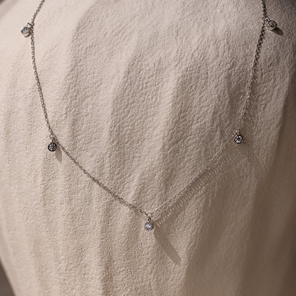 The Diamond Station Necklace, featuring delicate pendants, is shown on a textured stone—an elegant, timeless accessory that adds modern sophistication to any look.
