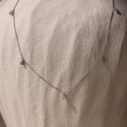 The Diamond Station Necklace, featuring delicate pendants, is shown on a textured stone—an elegant, timeless accessory that adds modern sophistication to any look.