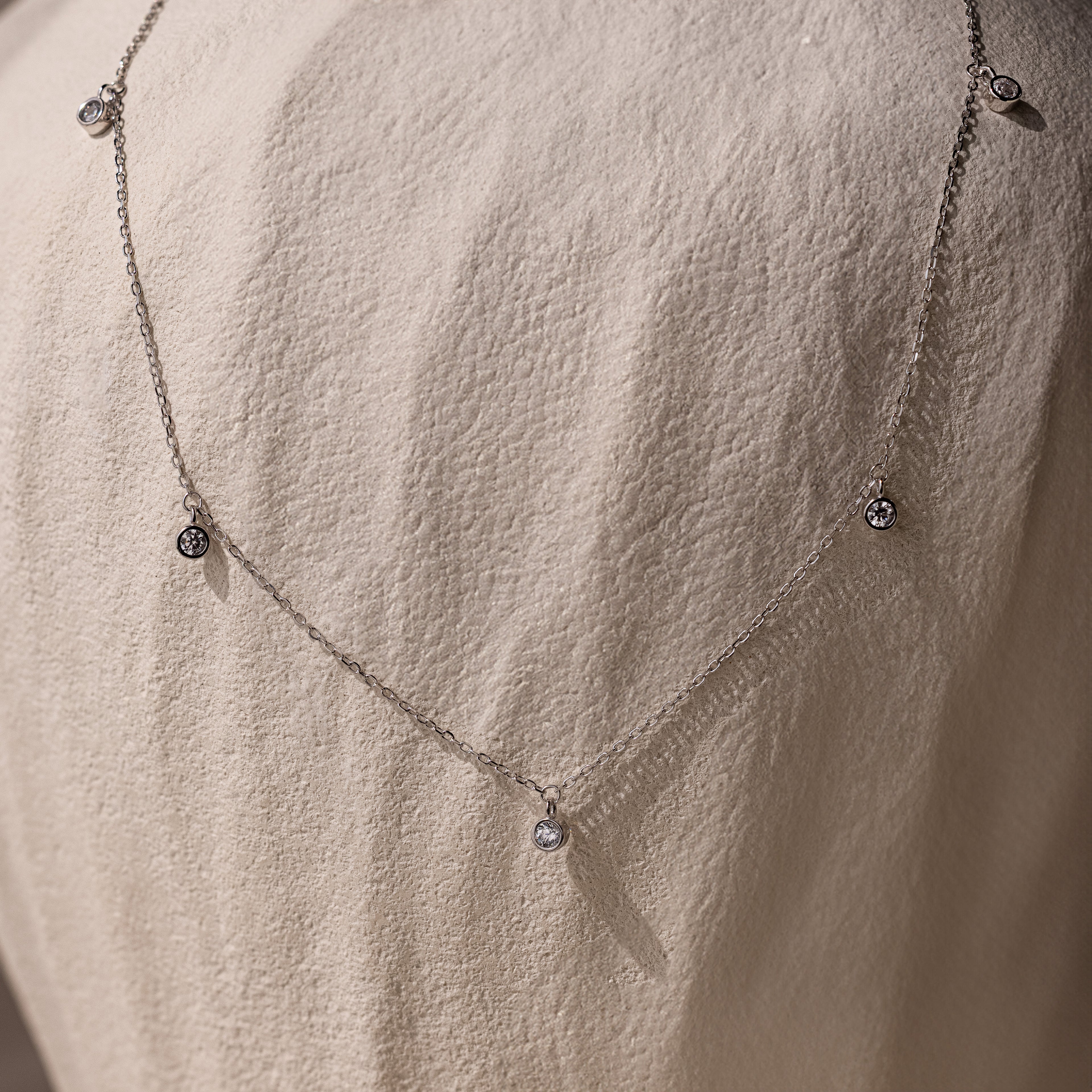 The Diamond Station Necklace, featuring delicate pendants, is shown on a textured stone—an elegant, timeless accessory that adds modern sophistication to any look.