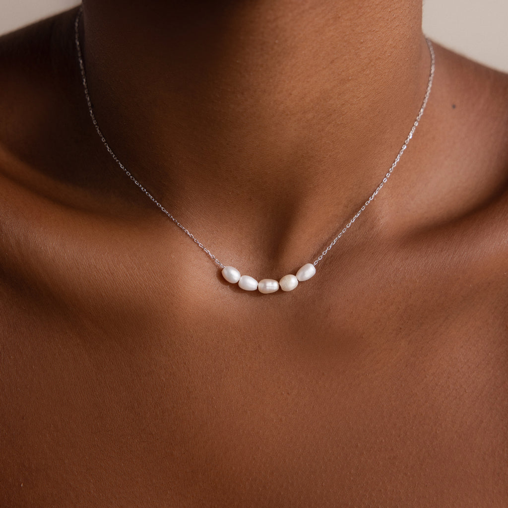 A close-up of a person wearing the Pearl Bead Necklace, featuring five small white pearls on a fine chain—an elegant gift for bridesmaids.