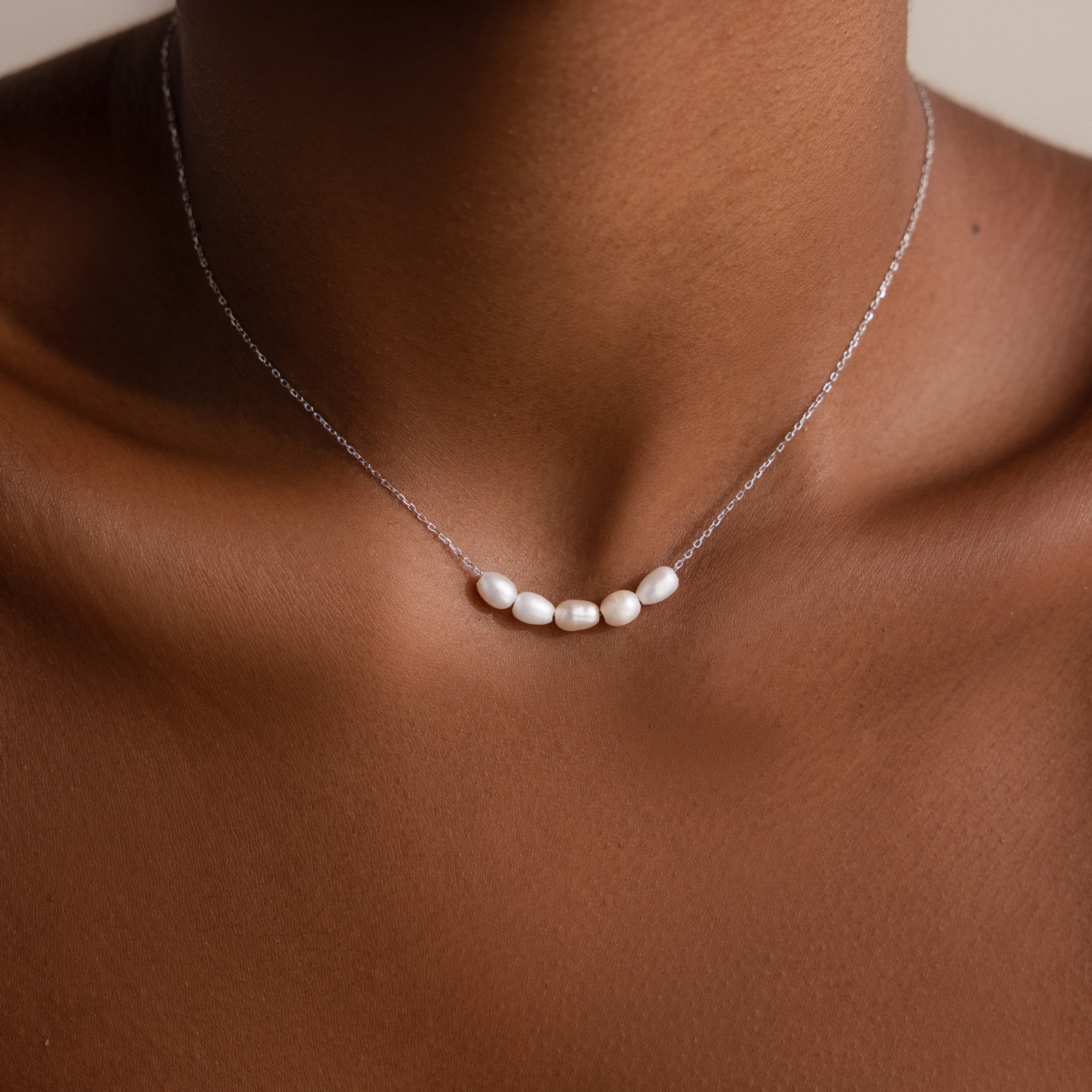 A close-up of a person wearing the Pearl Bead Necklace, featuring five small white pearls on a fine chain—an elegant gift for bridesmaids.