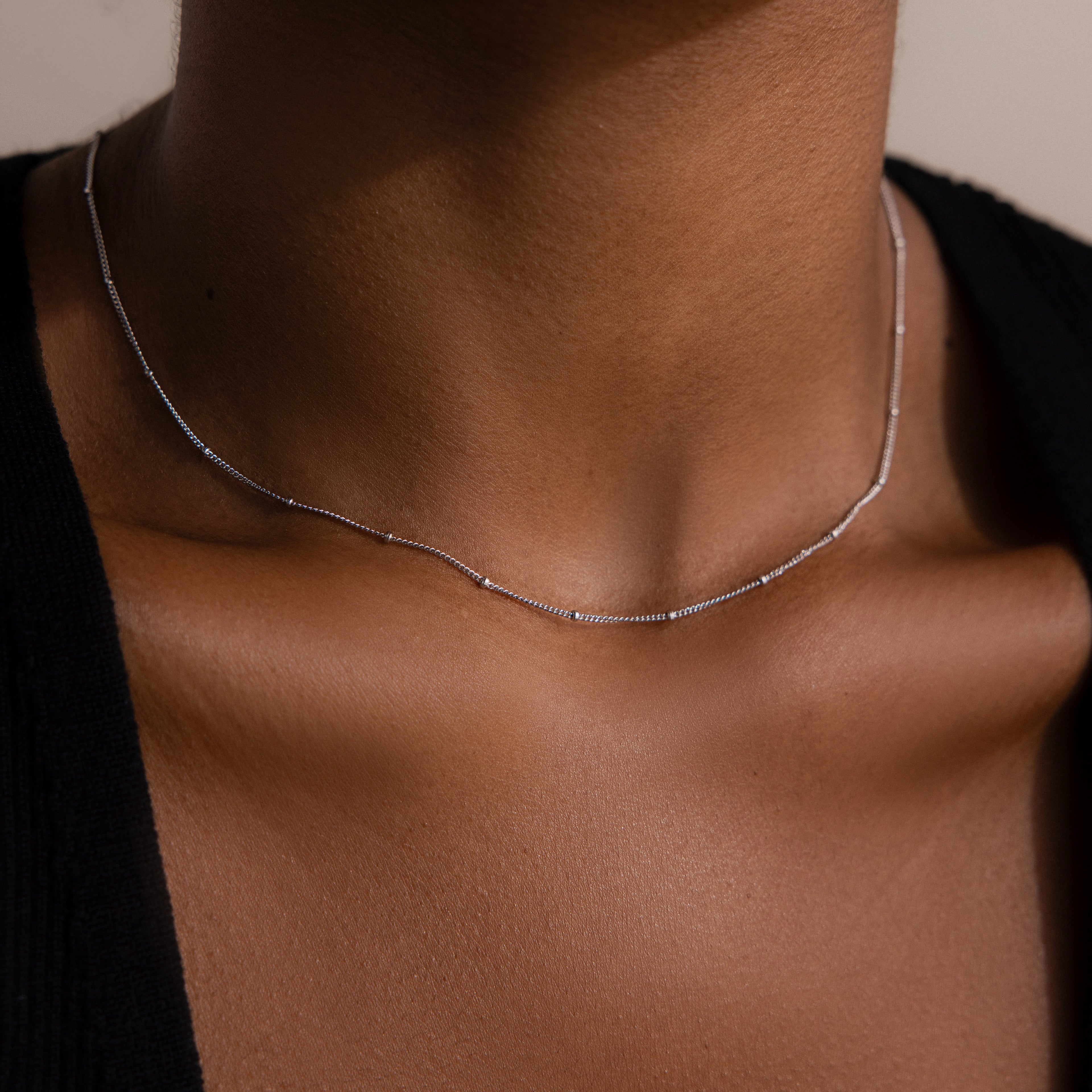 A close-up of someone wearing the Satellite Necklace, a delicate silver chain against bare skin and a black top—perfect for effortless layering looks.