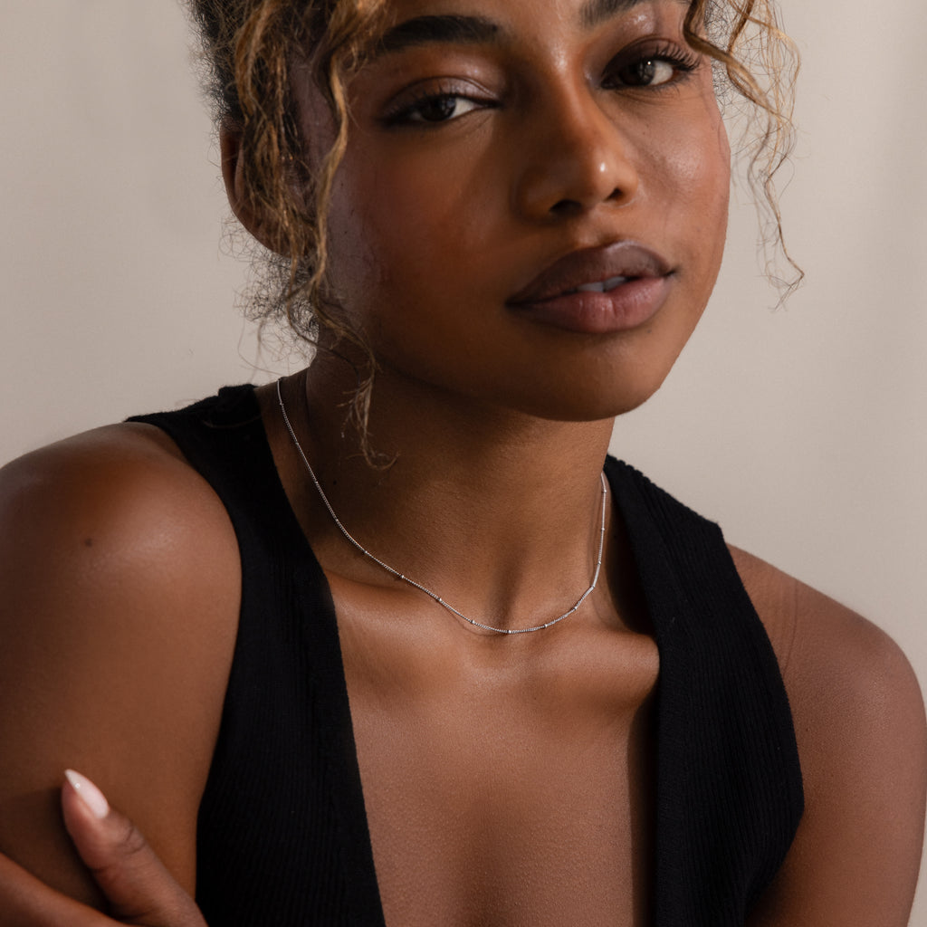Woman with curly hair wearing a black sleeveless top and the Satellite Necklace in Silver—perfect for layering or adding an elegant touch when worn alone.