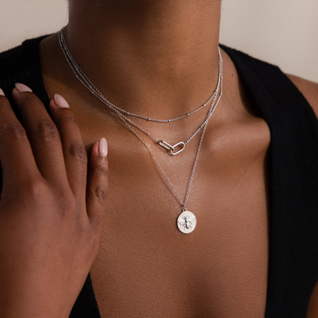 A woman in a black sleeveless top touches her collarbone while wearing the Linked Pendant Necklace in Silver, styled with other layered silver necklaces.