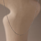 The Satellite Necklace in Silver features a delicate beaded chain, shown on a softly blurred neutral backdrop—an effortless layering piece for any style.