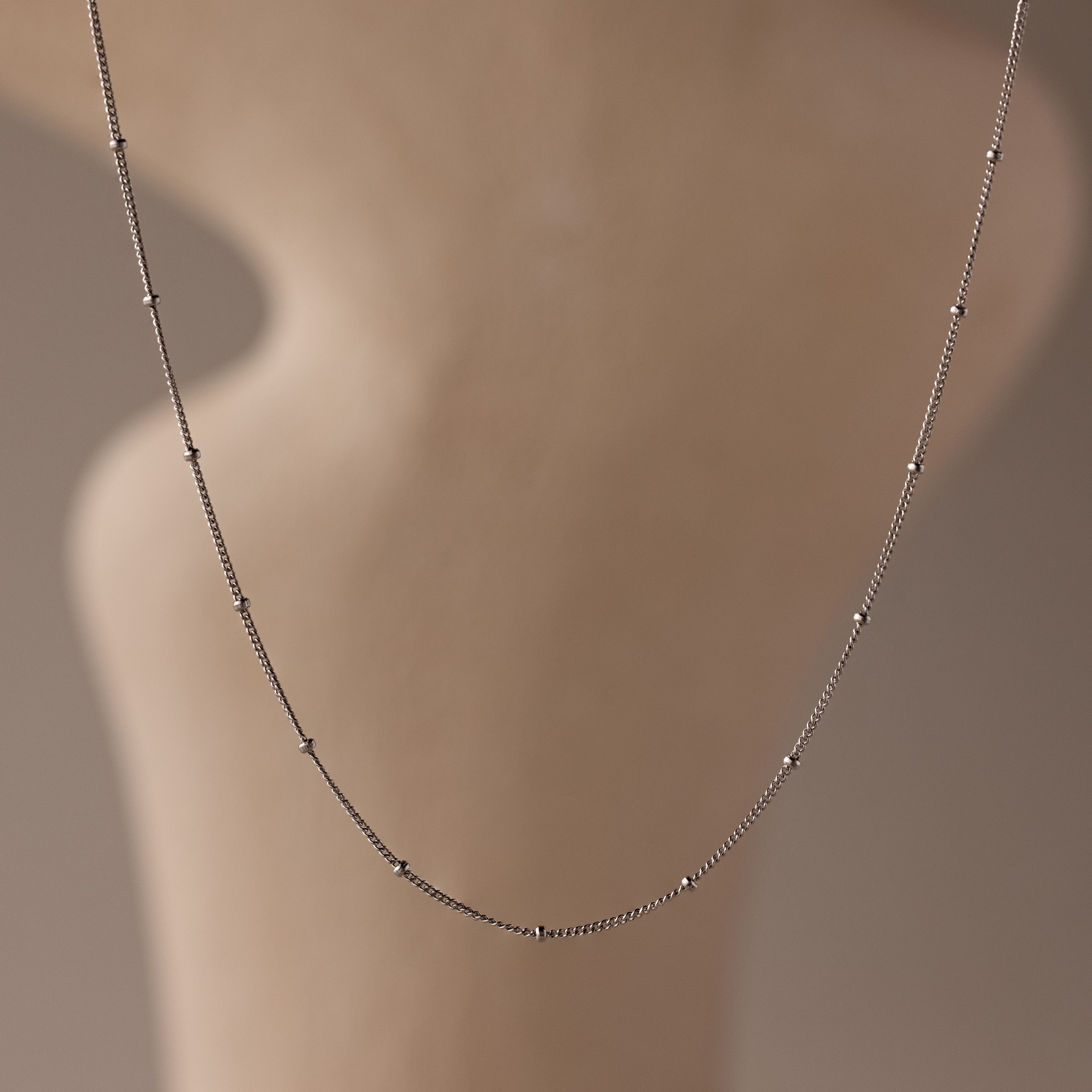 The Satellite Necklace in Silver features a delicate beaded chain, shown on a softly blurred neutral backdrop—an effortless layering piece for any style.