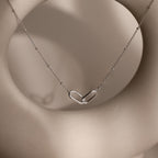 Linked Pendant Necklace featuring a heart-shaped linked pendant on a delicate chain, shown against a soft beige circular background.