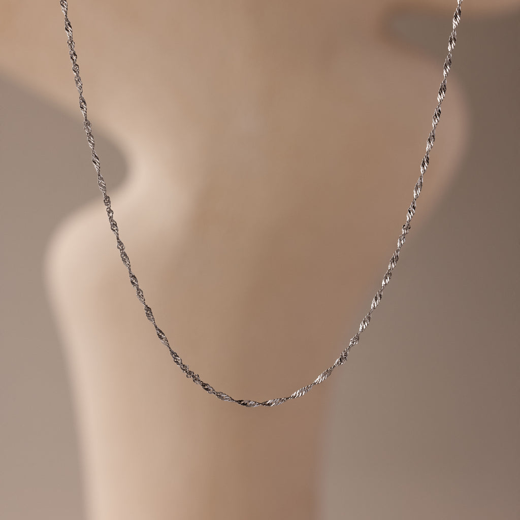 The Singapore Twist Necklace in Silver is showcased against a softly blurred, neutral background.