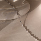 The Singapore Twist Necklace in Silver is displayed elegantly on a smooth, light stone surface.