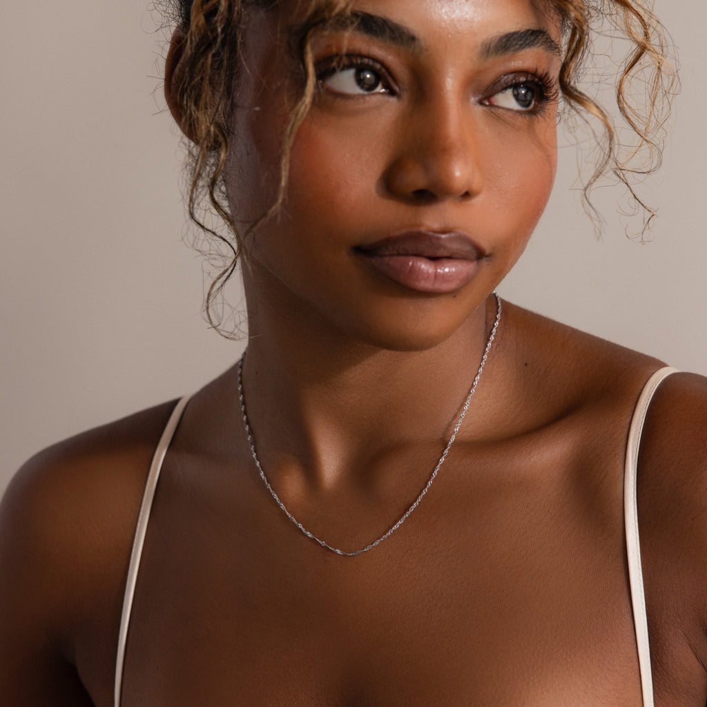 Woman with curly hair, in a thin strap top and a delicate Singapore Twist Necklace, looks off to the side.