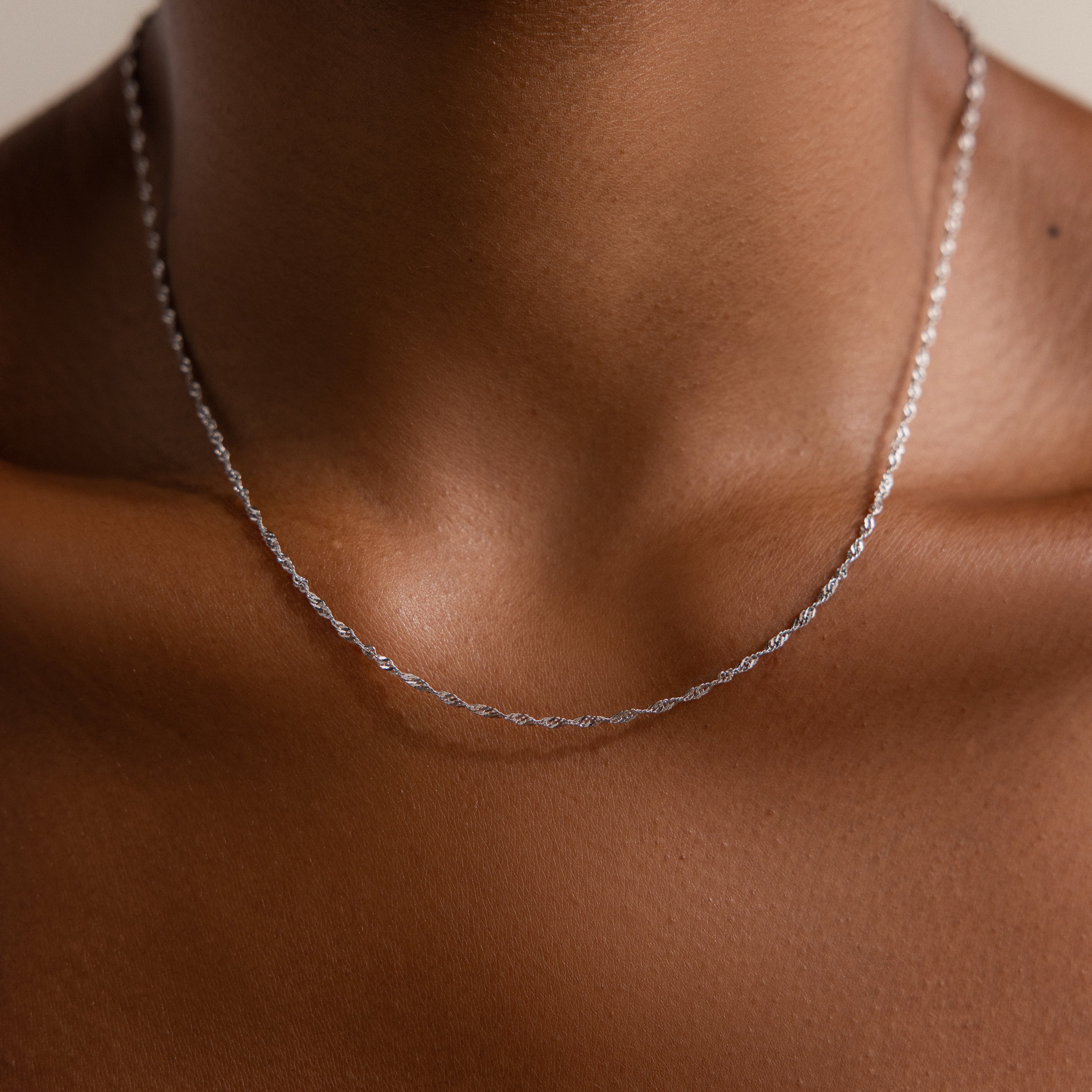 The Singapore Twist Necklace in Silver rests delicately on a person’s neck and upper chest, shining against smooth brown skin.
