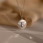 The Bee Coin Necklace in Silver features a round pendant with a raised bee design and is perfect for layering on any occasion. Displayed against a soft beige background.