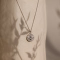 Bee Coin Necklace in Silver featuring a delicate bee design, ideal for layering. Displayed on a textured background with leafy shadows.