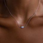 The Opal Eye Necklace, featuring a delicate silver pendant shaped like an eye, rests gracefully on a womans neck against brown skin.