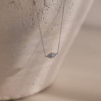 The Opal Eye Necklace in Silver features a delicate blue gemstone pendant, shown on a textured, light background—an elegant piece perfect as your lucky talisman.