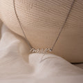 The Mrs. Necklace in Silver with a Mrs pendant is displayed on soft white fabric next to a ceramic vase—an ideal, thoughtful wedding gift for the bride-to-be.