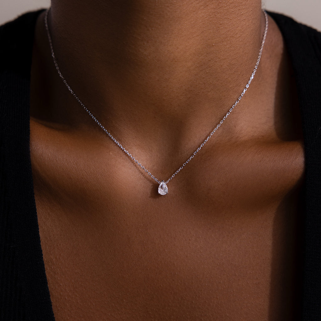 A close-up of a woman wearing the Rae Diamond Necklace in Silver, featuring a delicate chain and a small teardrop-shaped diamond pendant.