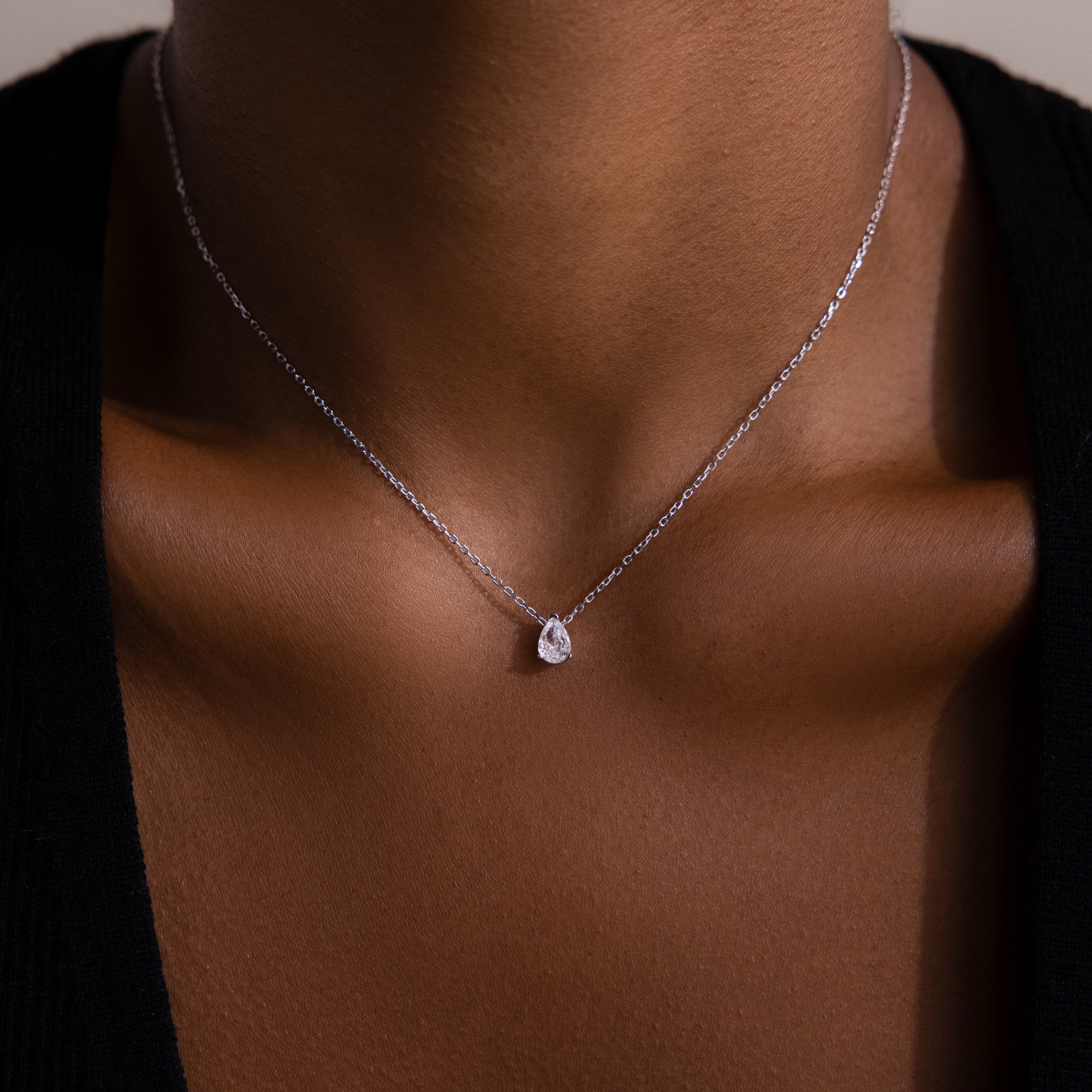 A close-up of a woman wearing the Rae Diamond Necklace in Silver, featuring a delicate chain and a small teardrop-shaped diamond pendant.