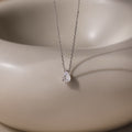 The Rae Diamond Necklace features a delicate silver chain with a teardrop diamond pendant, showcased on a smooth beige background—an elegant and exquisite jewelry piece.