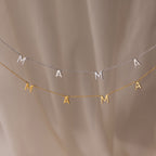 The Mama Letter Necklace—available in gold or silver—is elegantly displayed on a soft beige background, making it a perfect gift to celebrate motherhood.