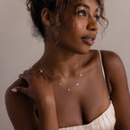 Woman in a cream dress wears the Mama Letter Necklace, looking to the side—a thoughtful gift for moms that celebrates motherhood.