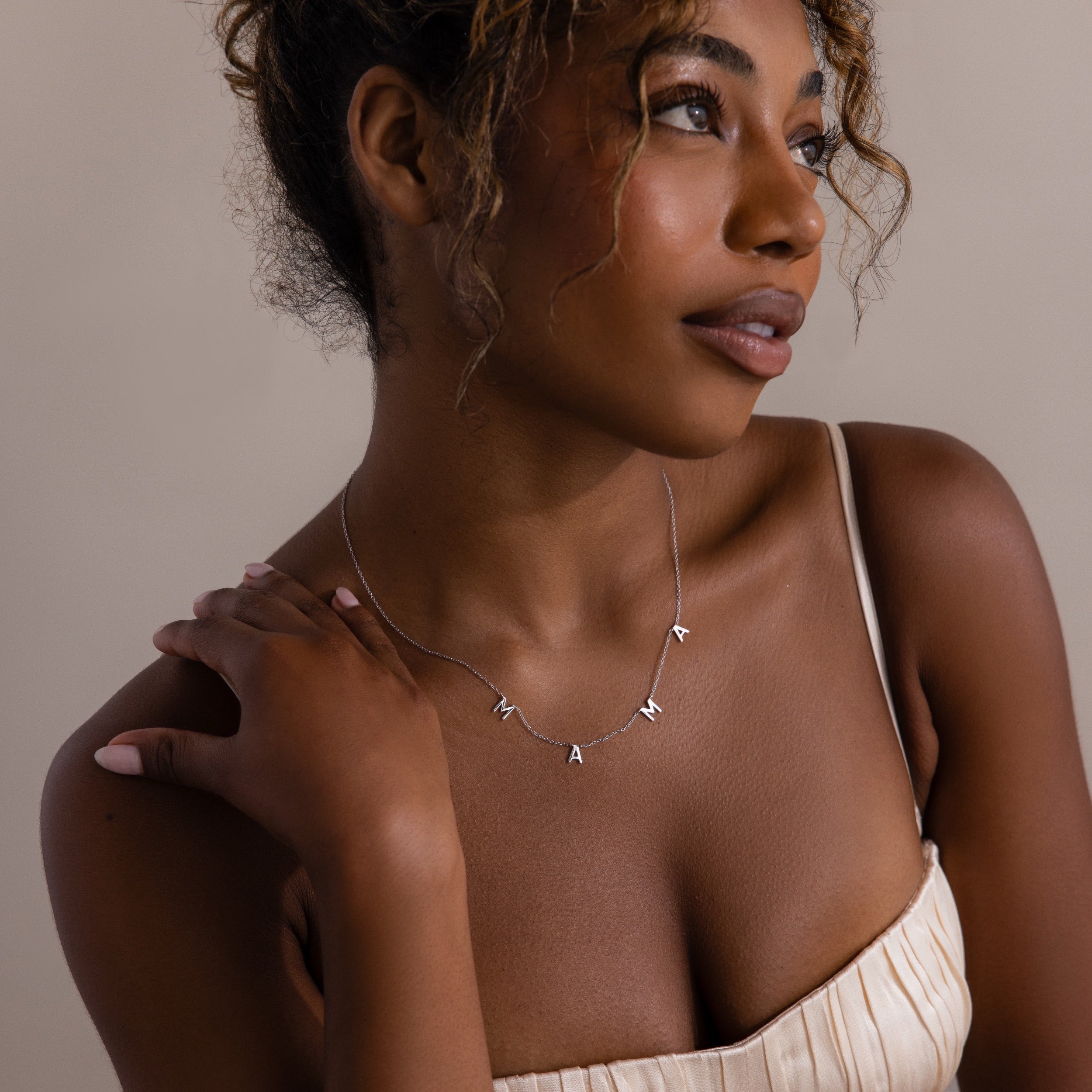 Woman in a cream dress wears the Mama Letter Necklace, looking to the side—a thoughtful gift for moms that celebrates motherhood.