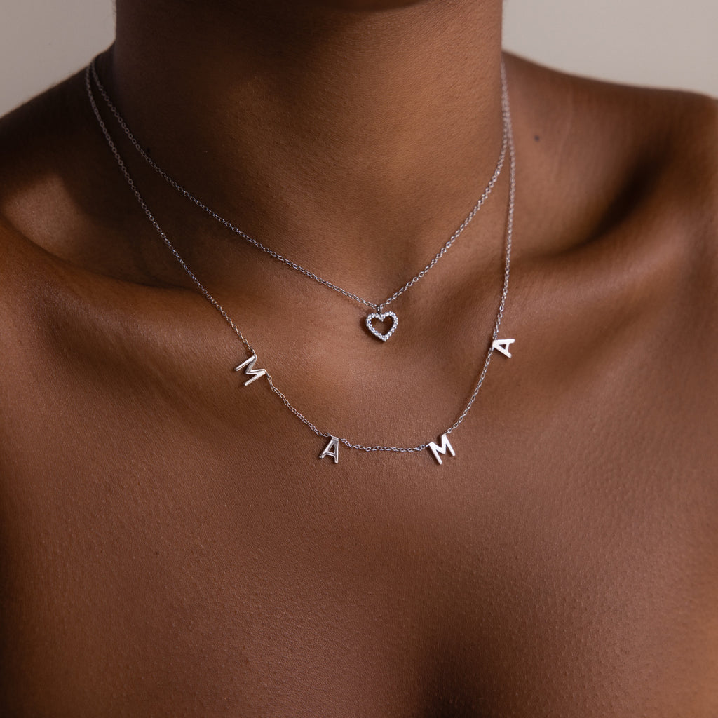 A woman wears two silver necklaces—one spells MAMA, the other is the Forever Pave Heart Necklace in Silver, perfect for everyday elegance or as heartfelt bridal jewelry.