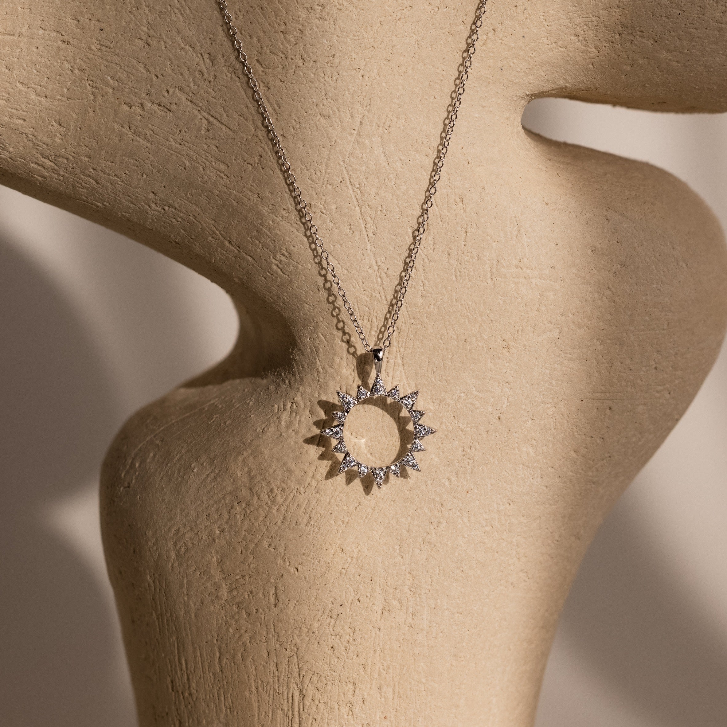 The Pave Sun Necklace in Silver, featuring sparkling pave accents, is displayed on a beige textured mannequin bust.