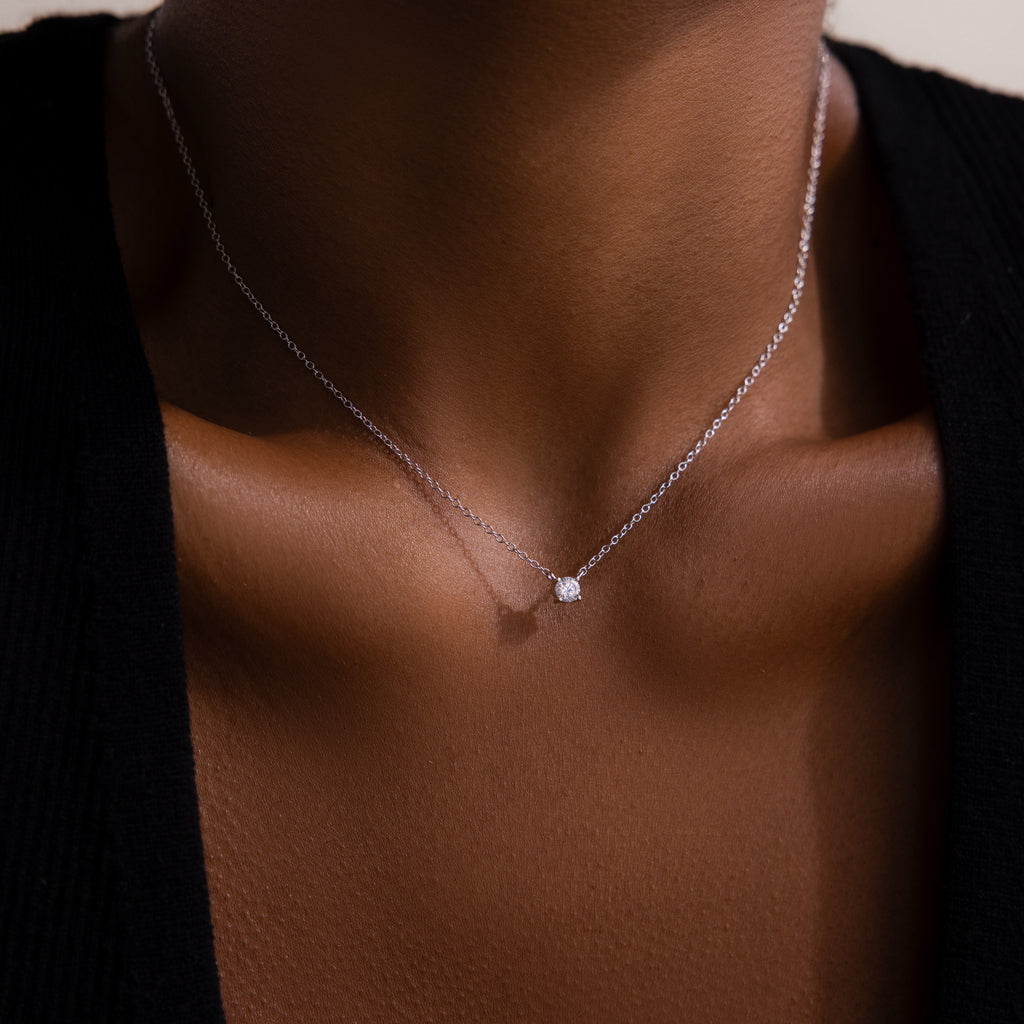 A close-up of the Dainty Diamond Necklace in Silver with a solitaire diamond pendant on someone wearing a black top—an elegant Christmas gift choice.