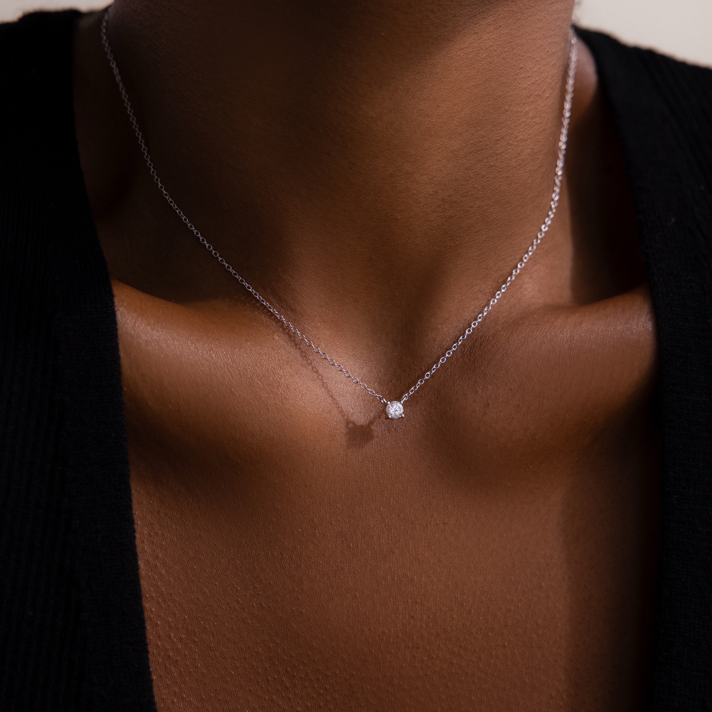 A close-up of the Dainty Diamond Necklace in Silver with a solitaire diamond pendant on someone wearing a black top—an elegant Christmas gift choice.