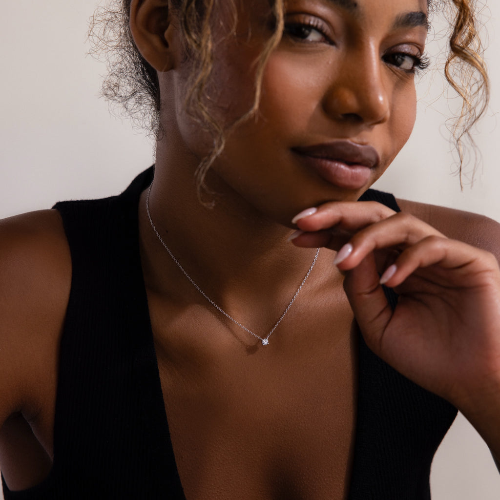 A woman in a black top wears the Dainty Diamond Necklace, gazing thoughtfully with her hand near her chin—a perfect gift idea for Christmas.