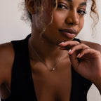 A woman in a black top wears the Dainty Diamond Necklace, gazing thoughtfully with her hand near her chin—a perfect gift idea for Christmas.