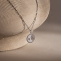 The Gabi Coin Necklace features a round sun and star pendant, displayed on a textured ceramic vase.