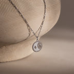 The Gabi Coin Necklace features a round sun and star pendant, displayed on a textured ceramic vase.