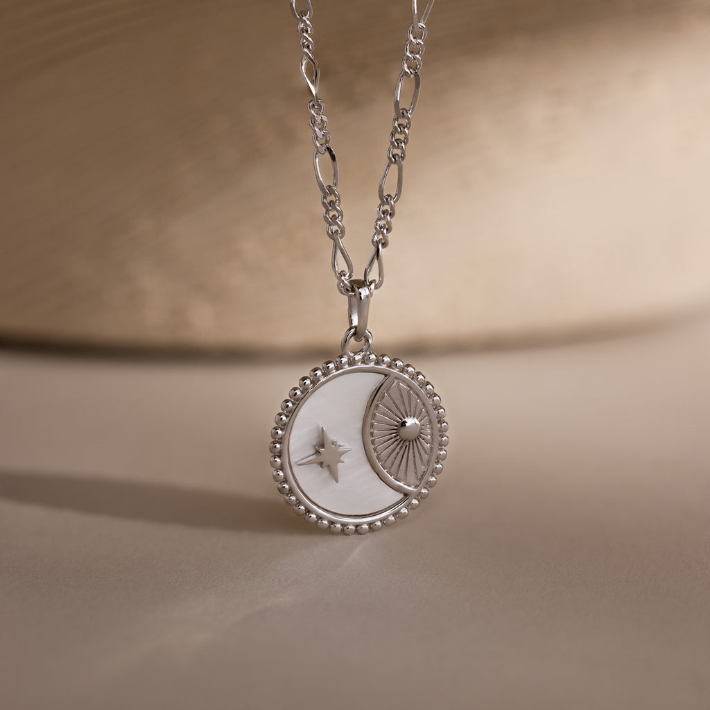 The Gabi Coin Necklace in Silver features a moon and star design with a beaded edge, adding minimal vintage charm—ideal for subtle style. Displayed on a neutral background.