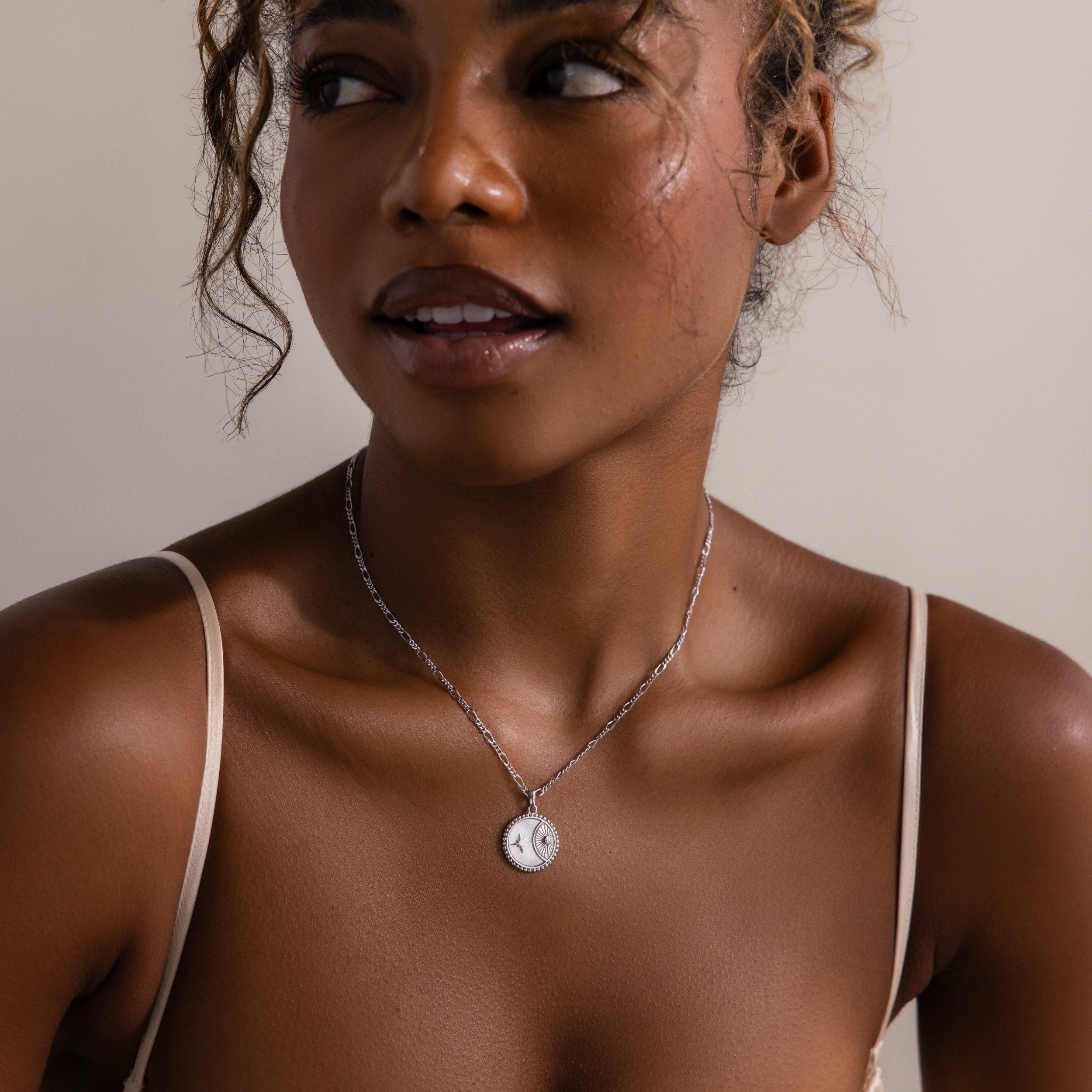Woman wearing the Gabi Coin Necklace in Silver and a beige strap top, looking slightly to the side and smiling softly.