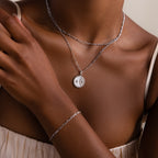 A woman wears minimal jewelry—layered silver necklaces, including the Gabi Coin Necklace in Silver, plus a matching silver bracelet.